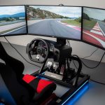 Où essayer un simulateur de course automobile dans le Finistère ? Cockpit moderne de simulateur de course automobile avec volant à retour de force, pédalier et triple écran montrant un circuit réaliste dans une ambiance intérieure éclairée de bleu.